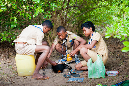 Three young boy scout are cooking under a tree during a camp.